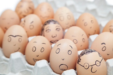 Various facial expressions painted on brown eggs in egg carton