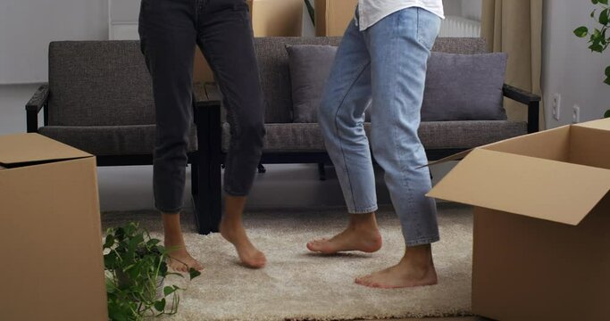 Close-up of part of human body of male and female legs in jeans dancing on floor in new house surrounded by cardboard boxes. Cropped shot of feet of two persons step make active movements on carpet