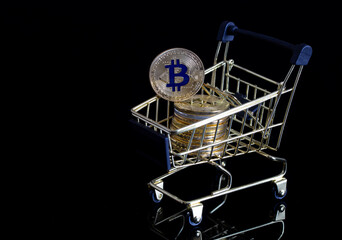 Fototapeta na wymiar Bitcoins in gold color in a consumer's basket on a black background. Cryptocurrency, digital money and electronic payments.