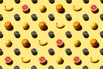 Trendy pattern made with fresh fruits on bright light yellow background. Flat lay. Minimal creative concept. Food background. Bananas, lemons, grapefruits, blueberries
