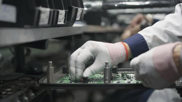 Manual assembly of components on a printed circuit board on conveyor. High tech factory facility.
