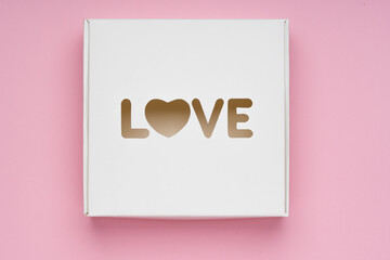 White box with word Love in shape of heart on rose background