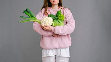 young woman holding a lot of green vegetables on a gray background