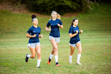 Three female soccer players running on field