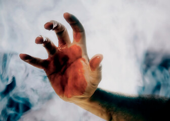 A smokey silhouette shot of the hand of a man, full of blood, searching for help or for a victim to...