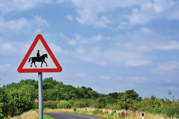 UK Road sign Accompanied horses or ponies likely to be in or crossing road ahead against a blue cloudy sky.