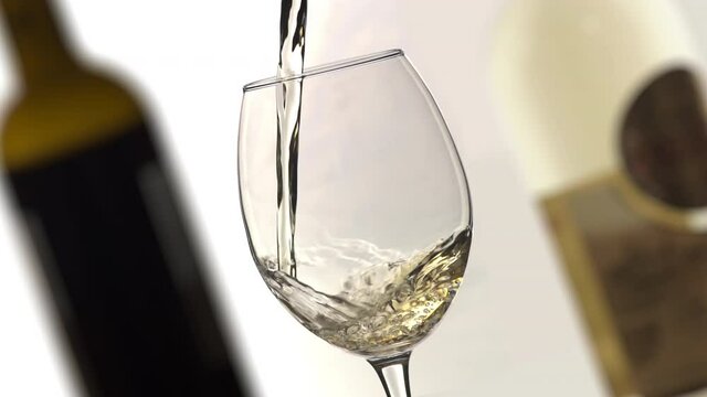 White wine pouring into wine glass slow motion angle shot, isolated background, wine bottles