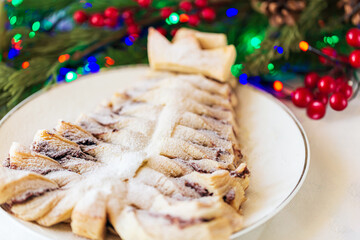 Puff pastry with chocolate filling is made in the shape of a Christmas tree. Christmas pastries on the background of fir branches with a bright Christmas garland. Selective focus 