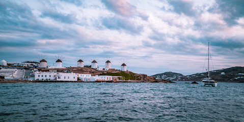 Panoramic sunset view of catamaran, windmills, and Aegean ocean in Mykonos Town (Chora) on the island of Mykonos, Cyclades