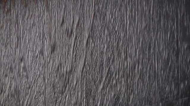 Black stone wall with water flowing down. Modern swimming pool or fountain in a shopping center. The movement of the camera from the bottom up.