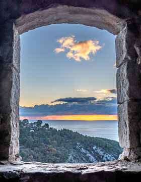 Lever de soleil et gros nuages sur la mer au travers d'une meurtri&egrave;re de la ville fortifi&eacute;e d'Eze sur la C&ocirc;te d'Azur