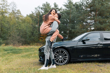 Beautiful young couple in tracksuits near their car. Happiness girl in the arms of her boyfriend