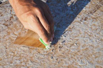 Crop image. Man surfer cleaning the surfboard from the old wax.