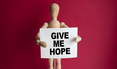 The wooden man holds a white sign with the text GIVE ME HOPE in his hands. The content of the...