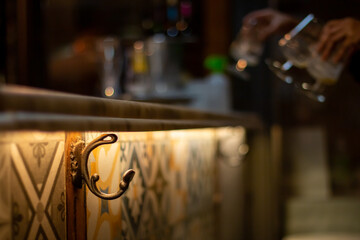 Fototapeta na wymiar Gancho para colgar los abrigos en la barra de un bar. Primer plano del detalle del gancho en una escena nocturna de un bar de Madrid, España.