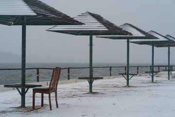 Blizzard in the touristic resort. Snowy Russian winter coming. River bank and parasols had been...