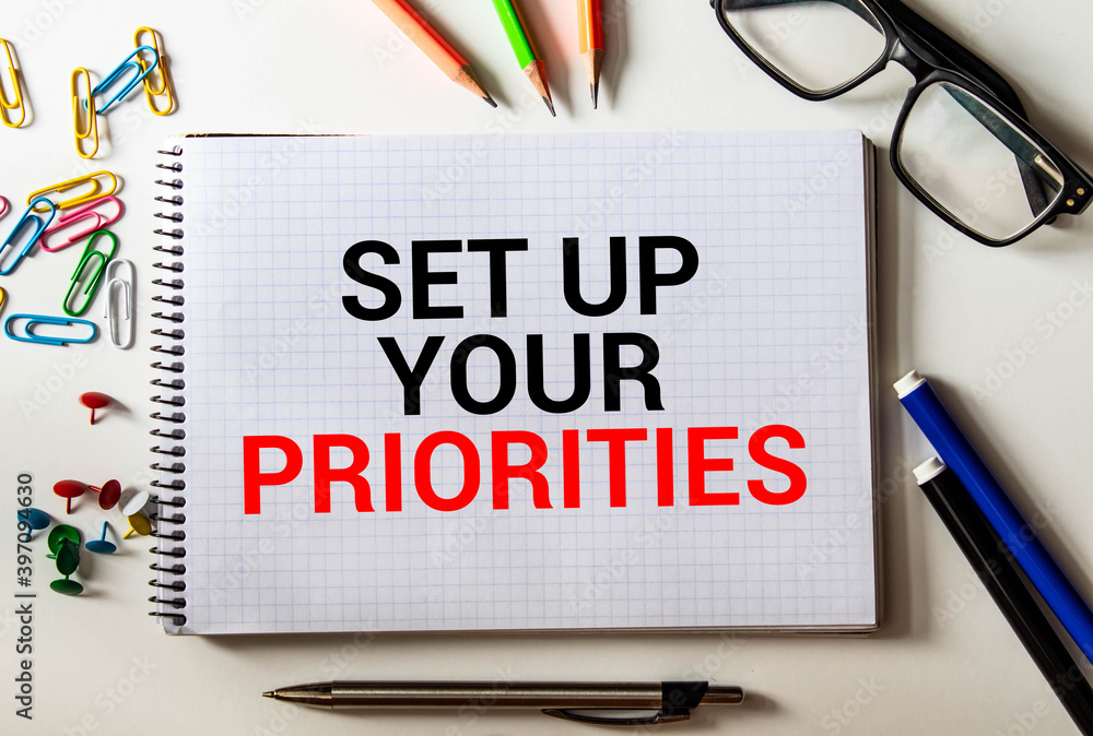 Poster laptop, red pen and notepad with text set up your priorities in the white background.