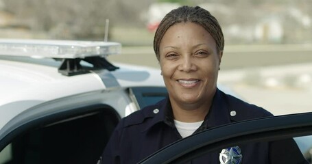 Police officer standing at police car and smiling