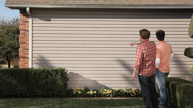 Caucasian men talking at exterior wall of house