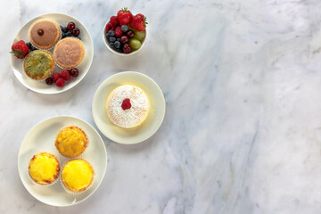 A top down view of an assortment of Japanese cheese tarts and a jiggle soft Japanese sponge cheesecake on a white marble worksurface. 