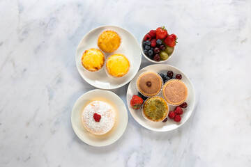 A top down view of an assortment of Japanese cheese tarts and a jiggle soft Japanese sponge cheesecake on a white marble worksurface. 