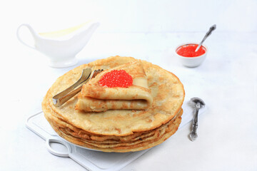 Delicious Russian pancakes with red caviar and a mug of milk on a bright light table. Healthy breakfast, natural products, traditional national cuisine, selective focus