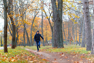 Fototapeta premium a boy running through the park and enjoys autumn, beautiful nature with yellow leaves