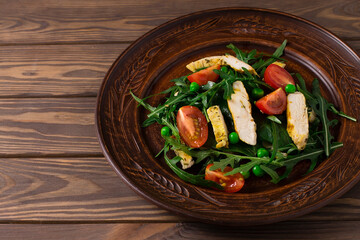 Healthy food, salad with chicken, cherry tomatoes, arugula and peas, in a plate, on a wooden background