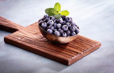 Bowl of fresh blueberries on rustic wooden board. Organic food blueberries and mint leaf for healthy lifestyle.