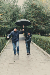 father and daughter running with umbrella, autumn city street, happy people together, parent and children