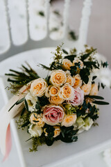 Fresh and beautiful bridal flower bouquet of colorful roses is lying on the white chair. Wedding floristry concept.
