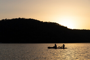 2 silhouettes in a canoe at sea at sunset