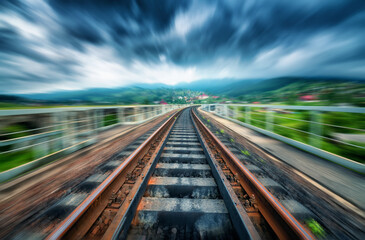Railroad bridge in mountains in overcast day with motion blur effect. Railway station and blurred background at moody sunset. Industrial landscape with railway platform in speed motion. Concept