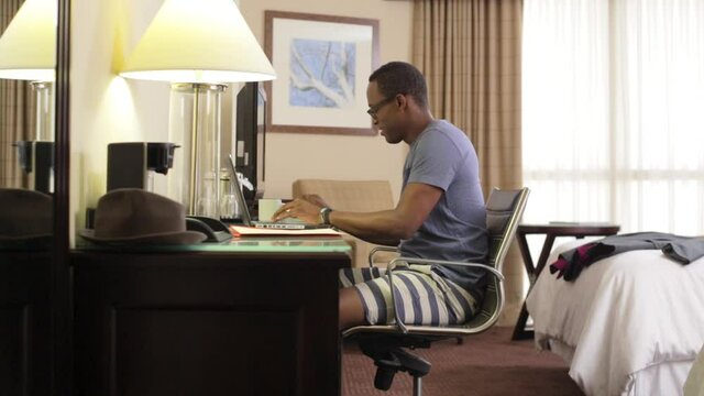 Black man drinking coffee and using laptop in hotel