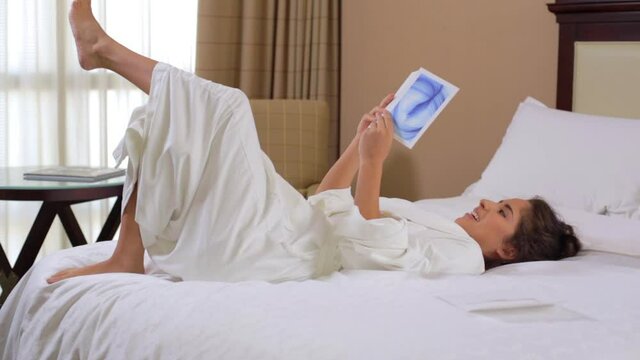 Hispanic woman in hotel reading spa menu on bed