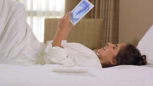 Hispanic woman in hotel reading spa menu on bed