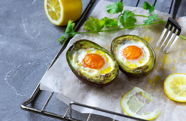 Keto diet dish: Baked avocado Boats with eggs and lemon on grey background