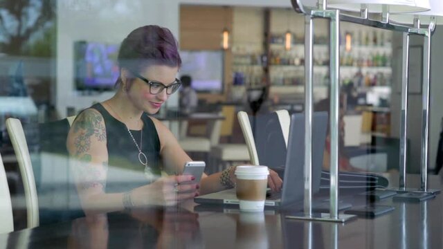 Caucasian businesswoman using laptop and cell phone in cafe