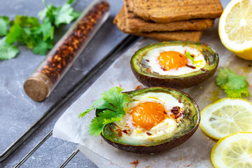 Keto diet dish: Baked avocado Boats with eggs and lemon on grey background