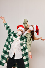 Woman in a medical mask and a man in a Christmas hat are gesturing with their hands on a light background