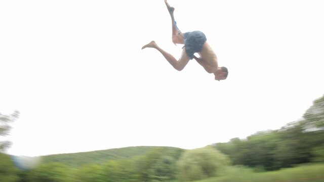 Friends watching boy swinging on rope swing into pond
