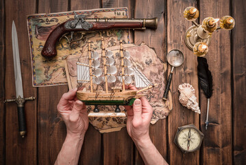 A small ship in the pirate hands on the wooden table background.