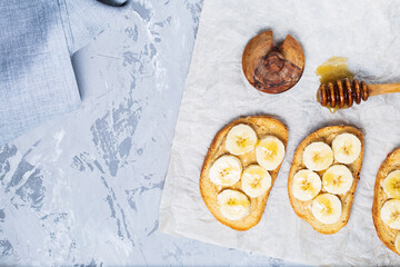 Delicious toasted sandwich bread with peanut butter, banana, honey on concrete background. Healthy, balanced traditional American school breakfast. Copy space, top view. Vegan sweet dessert