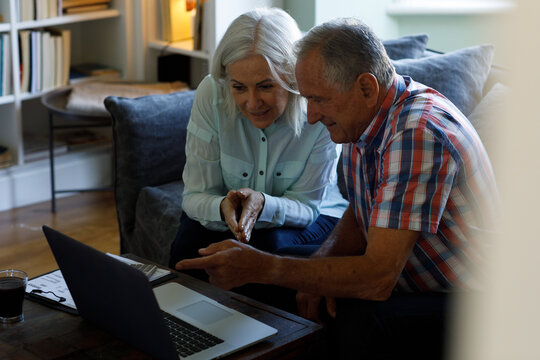 Senior caucasian couple using laptop while sitting on couch at home
