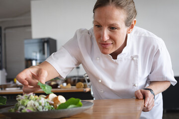 Senior female caucasian chef garnishing salad dish at restaurant kitchen