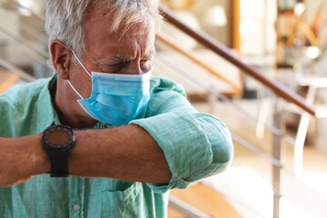 Senior caucasian man wearing face mask coughing into arm