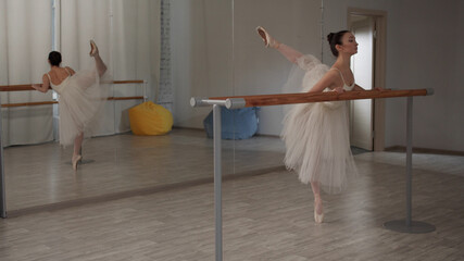 Aspiring ballerina in the ballet hall in a theatrical costume does a warm-up for the legs, moves...