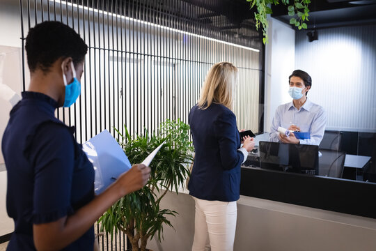 Diverse women wearing masks queing to reception, receptionist holding clipboard