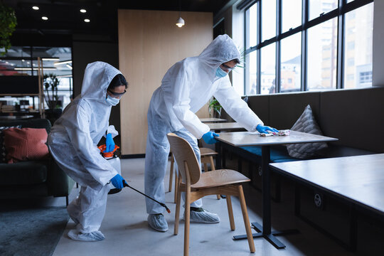 Health workers in protective clothing disinfecting creative office