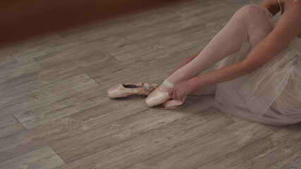 The ballerina sits on the floor, puts on pointe shoes and ties ribbons around her feet